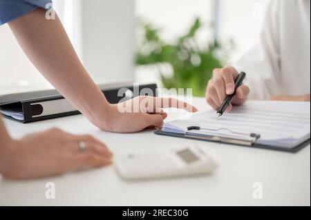 Nahaufnahme einer professionellen Geschäftsfrau oder einer weiblichen Führungskraft, die mit dem Finger auf einen Bericht zeigt, während sie mit ihrem Team im Büro über die Arbeit spricht. Stockfoto