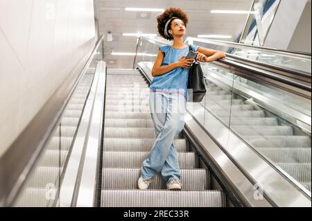 Eine schwarze Frau in voller Länge, die auf einer Rolltreppe in einer leichten U-Bahn steht Stockfoto