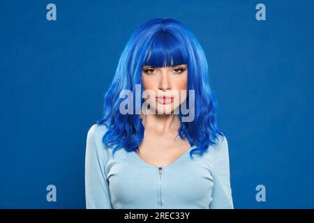 Porträtfoto einer Frau mit blauem Haar, die im Studio vor einem lebendigen Hintergrund in die Kamera schaut Stockfoto