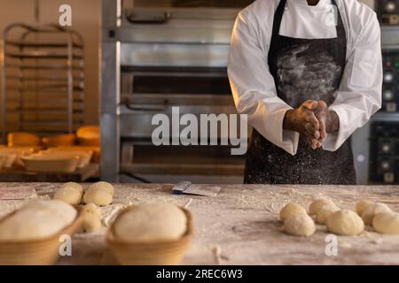 afroamerikanischer Bäcker in der Bäckerei-Küche klatscht Hände mit Mehl, Kopierraum Stockfoto