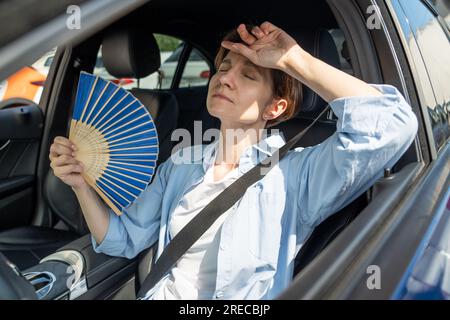 Erschöpfte Frau mittleren Alters fährt Autowellen blauer Fan leidet an Stau im Verkehr. Stockfoto