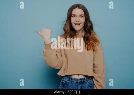 Amüsiert hübsche junge Frau mit Omelhaar, in lässigem hellbraunen Pullover und Jeans, mit dem Finger auf etwas zeigen, um Aufmerksamkeit zu erregen. Wieder stehen Stockfoto