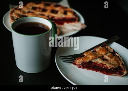Kirschkuchen mit einer Tasse normalen Kaffees auf dem schwarzen Tisch Stockfoto