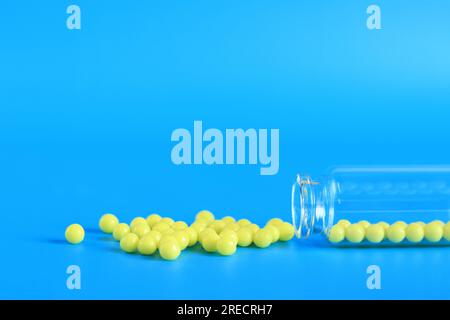 Gelbe Pillen werden aus einer Glasflasche auf blauem Hintergrund ausgeschüttet. Ascorbinsäure, Seitenansicht, Kopierraum. Gesundheitswesen, medizinische Pillen und Ernährung Stockfoto