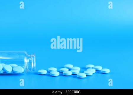 Blaue Pillen aus einer Glasflasche auf blauem Hintergrund. Vitamin-B-Komplex, Seitenansicht, Kopierraum. Gesundheitswesen, medizinische Pillen und Nahrungsergänzungsmittel Stockfoto