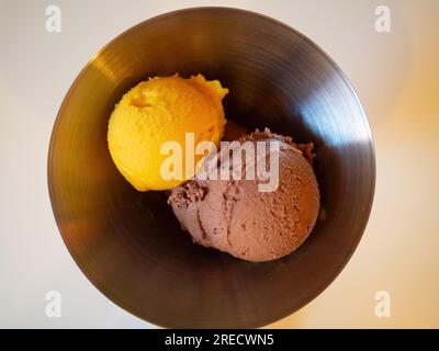 Zwei Kugeln Eiscreme in einer Metallschüssel - eine Kugel Mango und eine Kugel Schokolade. Stockfoto