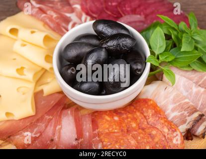 Eine Schüssel Oliven unter einer Vorspeise aus Wurst, Käse und grünem Basilikum. Gute Vorspeisen für Wein oder Bier. Schließen. Stockfoto
