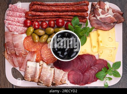 Draufsicht auf schwarze und grüne Oliven, Basilikum und Wurststücke, Fleisch, Käse. Flach liegend, Nahaufnahme. Stockfoto