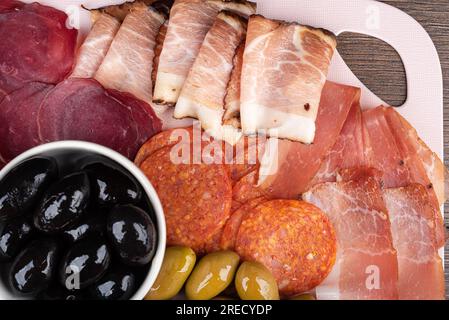 Blick von oben auf Speckscheiben, Prosciutto, Pastrami und Chorizo. Schwarze und grüne Oliven. Gute Vorspeisen für Wein oder Bier. Flach liegend, Nahaufnahme. Stockfoto