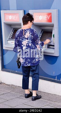 Finanzen, Banken, Geld, Frau, die Geldautomaten in der High Street benutzt, um Geld abzuheben. Stockfoto