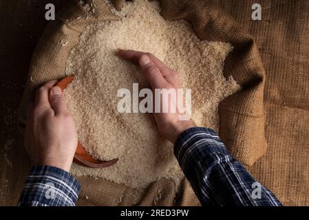 Menschliche Hände halten eine Hand voll Reis über einem Leinensack Stockfoto