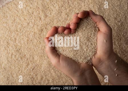 Menschliche Hände in Herzform, die eine Handvoll Reis auf dem Reishintergrund halten Stockfoto