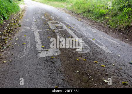 Norfolk, England. Ein langsames Schild, dreimal auf einer engen Landstraße gemalt. Niedriger Blickpunkt auf Bodenhöhe Stockfoto