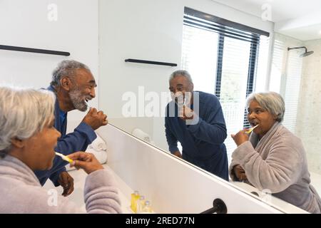 Glückliches älteres birassisches Paar, das zu Hause Bademäntel trägt und Zähne putzt Stockfoto