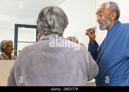 Glückliches älteres birassisches Paar, das zu Hause Bademäntel trägt und Zähne putzt Stockfoto