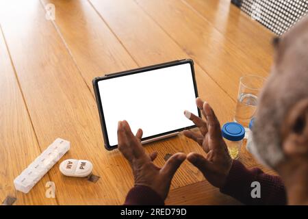 Ein ranghöchster birassischer Mann, der ein Videogespräch mit einem Arzt auf einem Tablet hat, mit Kopierraum, zu Hause Stockfoto