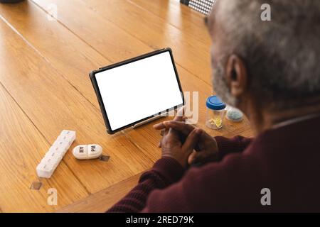 Ein ranghöchster birassischer Mann, der ein Videogespräch mit einem Arzt auf einem Tablet hat, mit Kopierraum, zu Hause Stockfoto