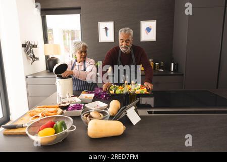 Älteres birassisches Paar in Schürzen, das Gemüse zubereitet und Lebensmittelabfälle in der Küche zu Hause kompostiert Stockfoto