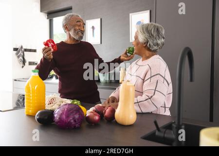 Glückliches älteres birassisches Paar, das zu Hause Gemüsesäcke in der Küche auspackt Stockfoto