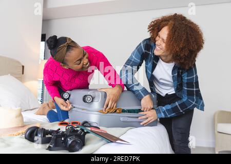 Glückliches, vielseitiges Paar, das den Koffer im Schlafzimmer zuhause zusammenschließt Stockfoto