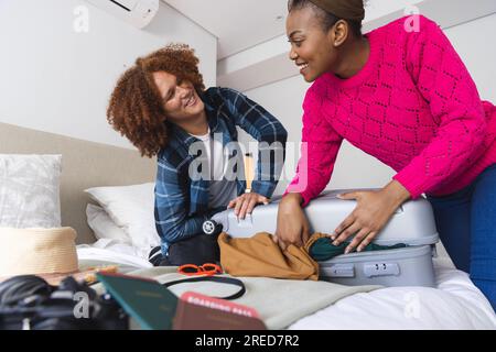 Glückliches, vielseitiges Paar, das den Koffer im Schlafzimmer zuhause zusammenschließt Stockfoto