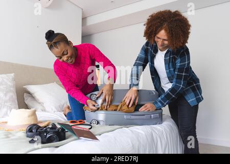 Glückliches, vielseitiges Paar, das den Koffer im Schlafzimmer zuhause zusammenschließt Stockfoto