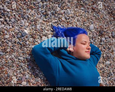Eine Frau trägt einen hellblauen Hoodie und Jeans in Übergröße. Blauhaarige Frau draußen im Park am Strand von Antalya. Kleidungsmodell, leerer Platz für Text o Design. Stockfoto