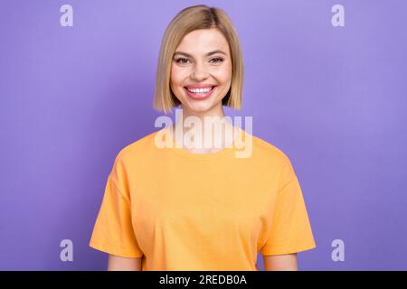 Nahaufnahme eines erstaunlichen jungen Mädchens, das eine Kamera sieht, die lächelt und ein gelbes T-Shirt trägt, isolierter lilafarbener Hintergrund Stockfoto