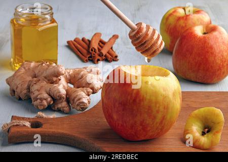 Roter Apfel und Löffel mit tropfendem Honig auf dem Hintergrund der Zutaten auf einem blauen Holztisch. Ich koche gebackene Äpfel mit Honig, Zimt und Ingwer Stockfoto