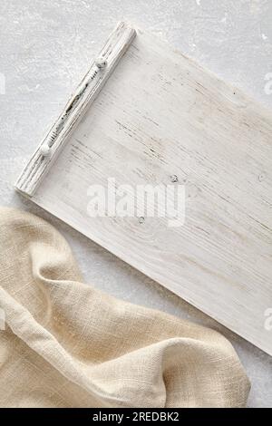 Weißes, aus Holz gestrichenes Serviertablett der Provence und grobe Bettwäsche Beige Küchentücher auf grauem Steintisch Blick von oben mit Kopierbereich Stockfoto