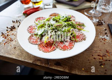 Rindercarpaccio. Borettanzwiebeln, sonnengetrocknete Tomaten, Trüffeldressing, Rucola-Salat, Parmesan-Käse. Italienische traditionelle Antipasti-Snacks für l Stockfoto