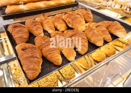 Frisches Gebäck auf der Theke im Geschäft. Im Ofen gebackene Croissants auf Backpapier mit Pergamentpapier. Süße Bagels, in einem heißen Ofen gebacken. Maki-Prozess Stockfoto