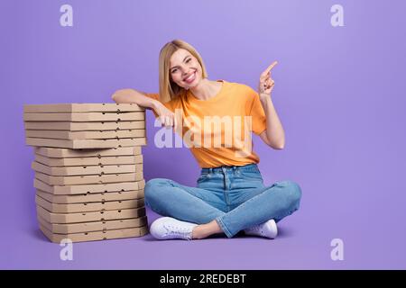 Ganzkörperfoto einer jungen blonden Marketing-Frau mit orangefarbenem T-Shirt, das die Finger-Modell-Pizzeria isoliert auf violettem Hintergrund zeigt Stockfoto