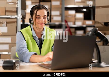 Porträt eines lächelnden Lagerpersonals, das einem Kunden mit einem Headset zuhört und mit ihm spricht, während er in einem Vertriebslager arbeitet. Weiblicher Anruf Stockfoto