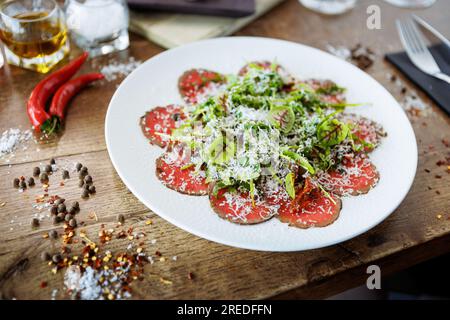 Rindercarpaccio. Borettanzwiebeln, sonnengetrocknete Tomaten, Trüffeldressing, Rucola-Salat, Parmesan-Käse. Italienische traditionelle Antipasti-Snacks für l Stockfoto