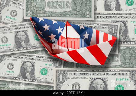 Ein Haufen amerikanische 1-Dollar-Banknoten mit einem Papierboot, gefaltet von US Stars and Stripes Flag. Stockfoto