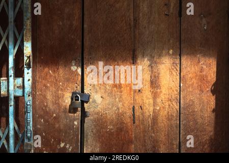 Altes goldenes Stahlschloss und beschädigte und verrostete Stahltür an Holztür. Verriegelt an Holztür mit altem Metallladen und Falttor. Alter Arbeitsauftrag Stockfoto