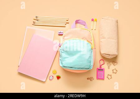 Stylischer Schulrucksack mit verschiedenen Schreibwaren auf orangefarbenem Hintergrund Stockfoto