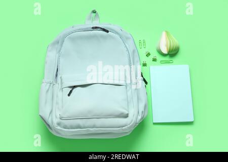 Stylischer Schulrucksack mit verschiedenen Schreibwaren auf grünem Hintergrund Stockfoto