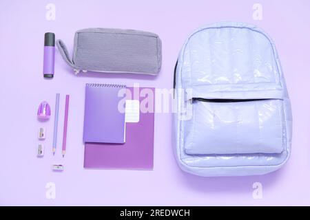 Lila Schulrucksack mit verschiedenen Schreibwaren auf lila Hintergrund Stockfoto