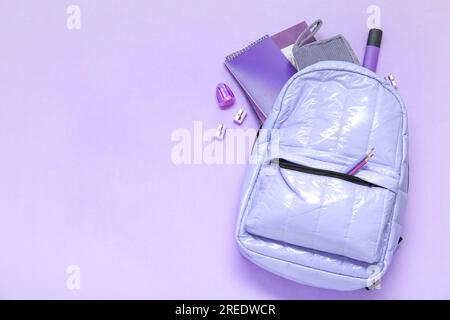 Lila Schulrucksack mit verschiedenen Schreibwaren auf lila Hintergrund Stockfoto