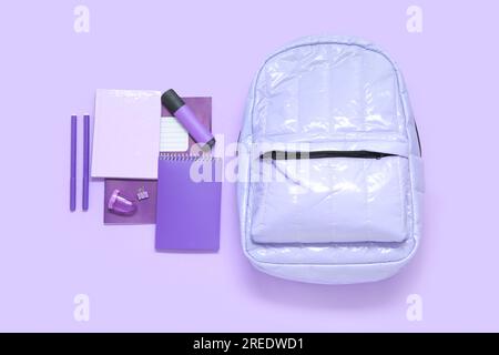 Lila Schulrucksack mit verschiedenen Schreibwaren auf lila Hintergrund Stockfoto