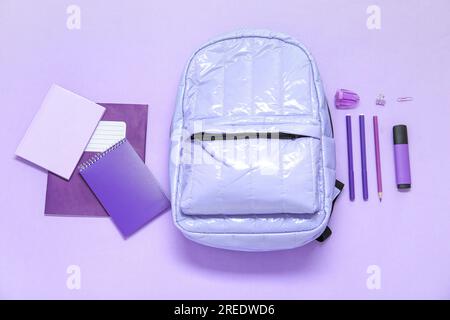 Lila Schulrucksack mit verschiedenen Schreibwaren auf lila Hintergrund Stockfoto
