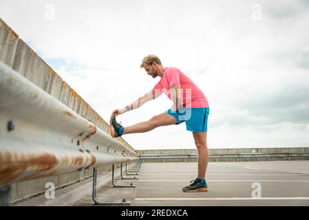 Sportlicher Mann mit Beindehnung im Freien Stockfoto