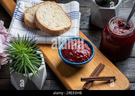 Frische hausgemachte Himbeermarmelade in einer Schüssel, serviert auf einer Holzplatte mit Brot Stockfoto