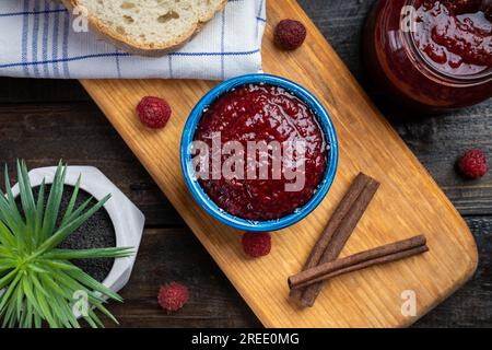 Frische hausgemachte Himbeermarmelade in einer Schüssel, serviert auf einer Holzplatte mit Brot Stockfoto