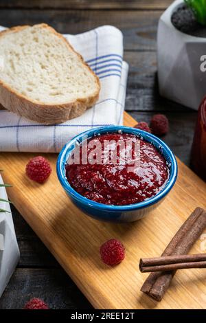 Frische hausgemachte Himbeermarmelade in einer Schüssel, serviert auf einer Holzplatte mit Brot Stockfoto