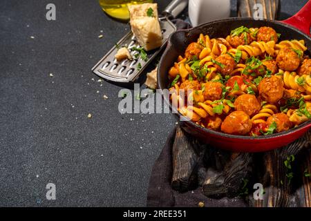 Fusilli-Pasta mit Fleischbällchen in Tomatengemüsesoße, auf dunklem Hintergrund mit Kräutern und geriebenem Käse, Kopierbereich von oben Stockfoto
