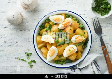 Traditioneller Kartoffelsalat mit Speck und Eiern in einer weißen Schüssel. Picknick-Food-Konzept. Schüssel mit warmem Kartoffelsalat. Deutscher Kartoffelsalat. Draufsicht. Stockfoto