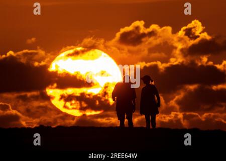 Isle Of Palms, Usa. 27. Juli 2023. Ein Paar, das vom Sonnenaufgang über dem Atlantischen Ozean am Strand am 27. Juli 2023 auf der Isle of Palms, South Carolina, umgeben ist. Eine anhaltende Hitzewelle über den Süden der USA bringt weiterhin extrem heißes, feuchtes Wetter in die Region. Kredit: Richard Ellis/Richard Ellis/Alamy Live News Stockfoto